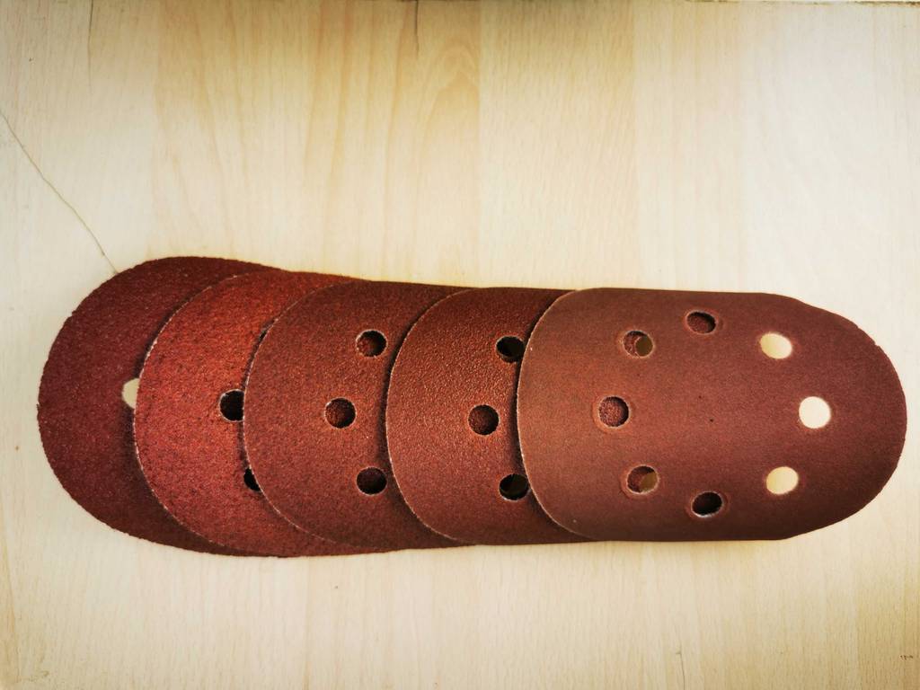 Mehrere verschiedene Schleifscheiben 125 mm liegen zum testen auf einem Holzbrett.