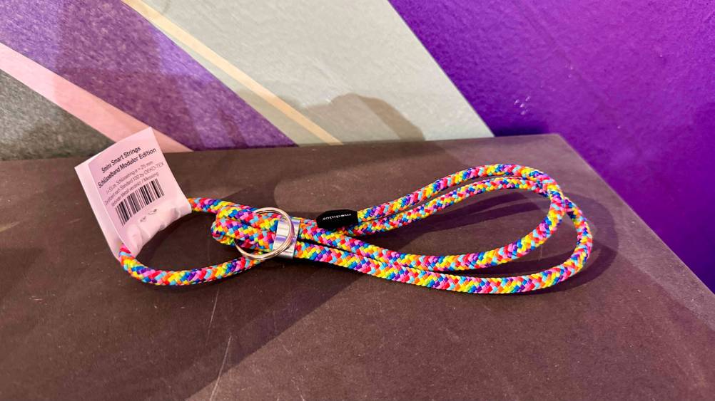 Das getestete Schlüsselband mit Etikett vor einer lila Wand.