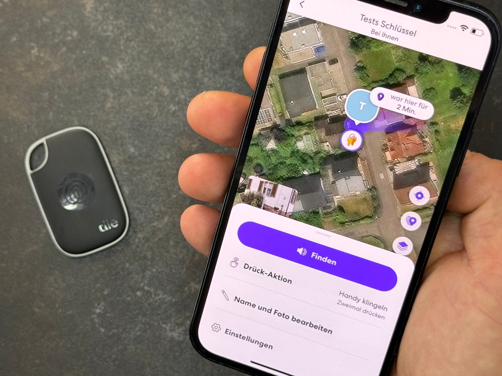 Eine Person hält ein Smartphone mit geöffneter App neben den getesteten Schlüsselfinder von Tile.