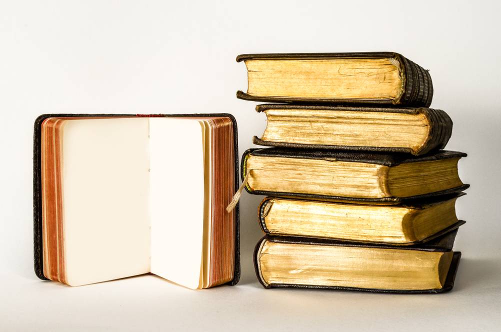 Mehrere Bücher, eines davon aufgeschlagen, mit Goldschnitt an den Seiten.