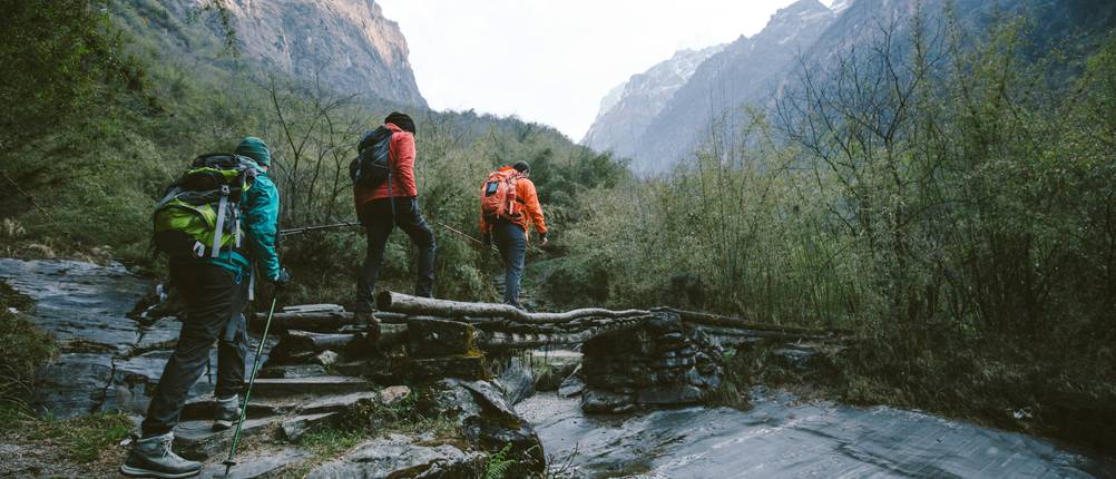 Trekkingschuhe Unisex im Test: drei Personen überqueren auf einer Trekkingtour einen Fluss.