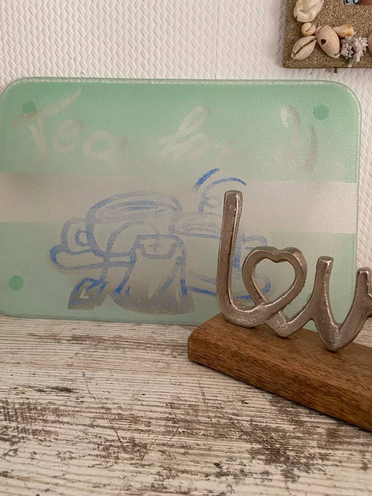 An einer dekorierten Wand lehnt das getestete Schneidebrett aus Glas auf einem Holztisch.