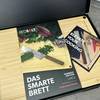 Das Redsalt Bambusbrett liegt geöffnet in der Verpackung mit Broschüre. Die Vorderseite zeigt Messer, Gemüse und das Produktlogo.
