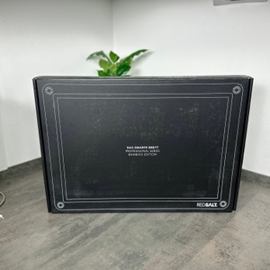 Die geschlossene Verpackung des Redsalt-Bambusbretts steht aufrecht auf einer Küchenarbeitsplatte. Auf der Vorderseite steht „Das smarte Brett“.