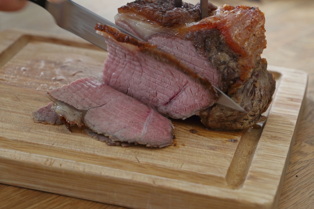 Roastbeef wird auf einem Holzschneidebrett mit Saftrille aufgeschnitten