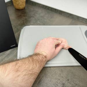 Eine Hand schneidet Hähnchenbrust auf dem Silit-Schneidebrett 21.4223.5354 mit einem schwarzen Messer.
