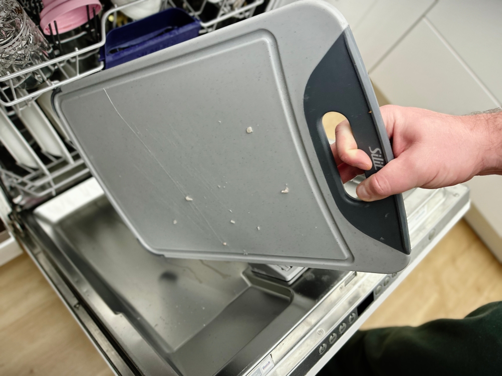 Das Silit-Schneidebrett 21.4223.5354 wird mit der Hand in die offene Spülmaschine gelegt. Die Oberfläche zeigt leichte Rückstände.