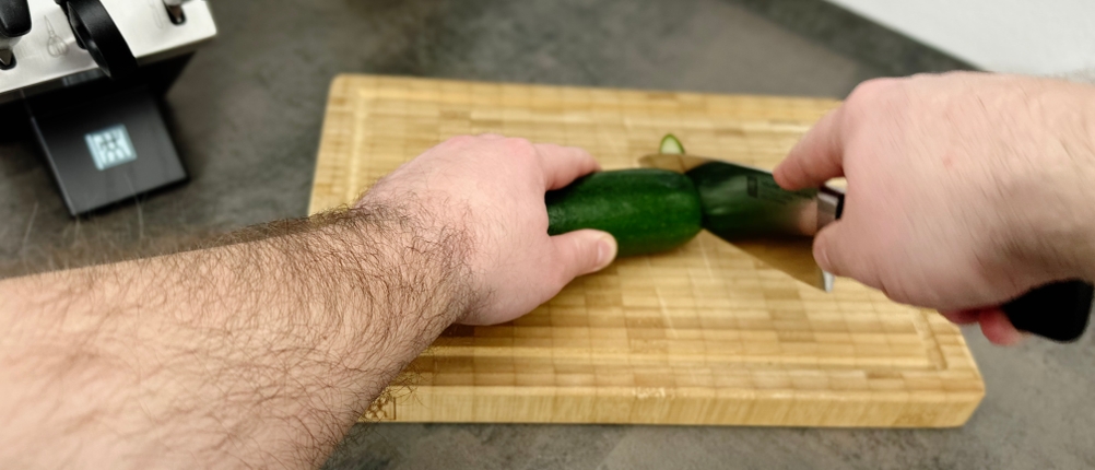 Eine Zucchini wird auf dem Zwilling-Schneidebrett 30772-100 mit einem Messer in Scheiben geschnitten.