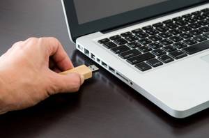 Eine Männerhand steckt einen getesteten 256-GB-USB-Stick in ein silbernes Notebook.