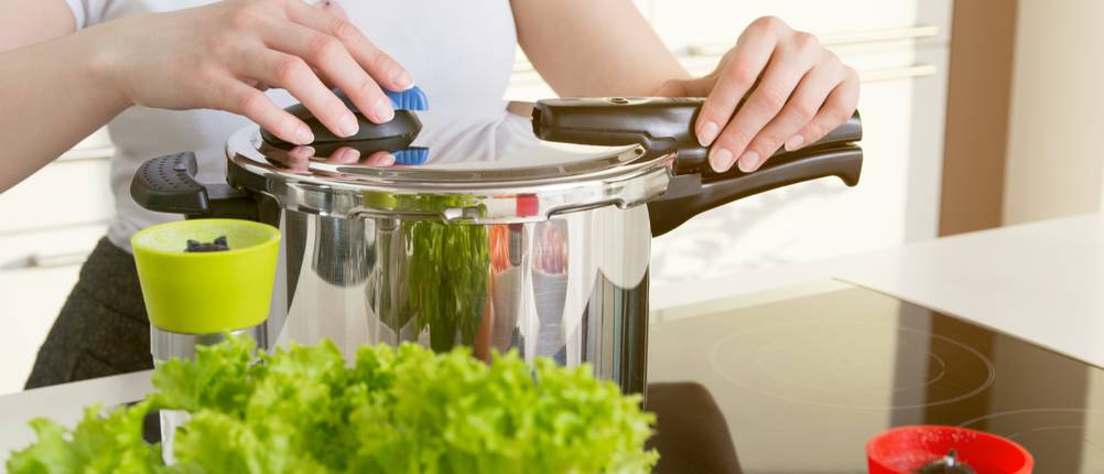 6-Liter-Schnellkochtopf im Test: Eine Frau bedient den Deckel eines Schnellkochtopfs aus Edelstahl. Im Vordergrund sind Salat und Gewürze zu sehen.