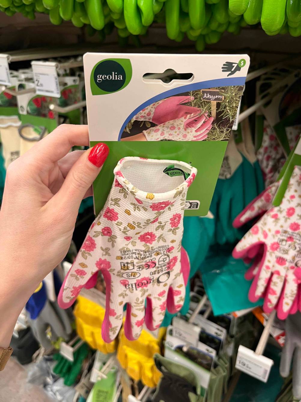 Eine Hand hält ein Paar getestete Schnittschutzhandschuhe vor einem Geschäftsregal.