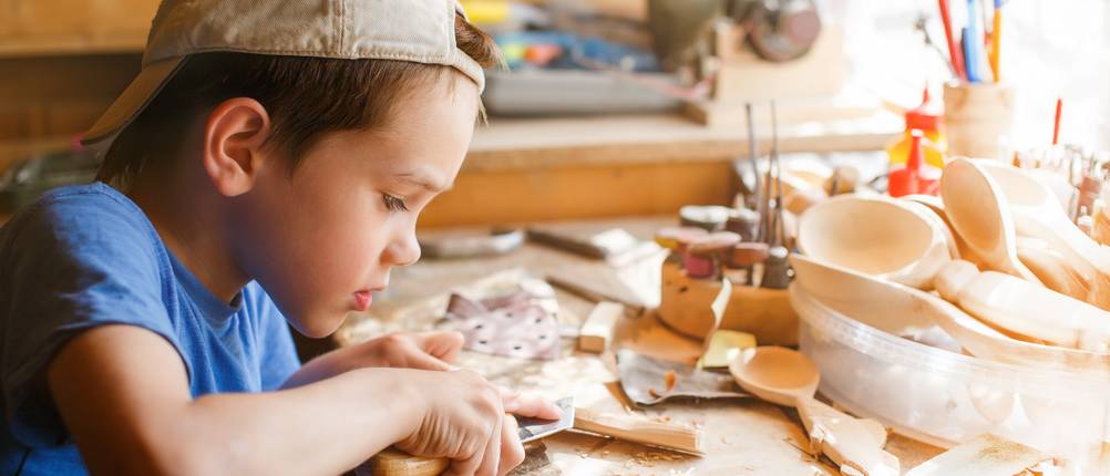 Schnitzholz-Test: Kind arbeitet in einem Workshop mit Holz und Schnitzmesser.