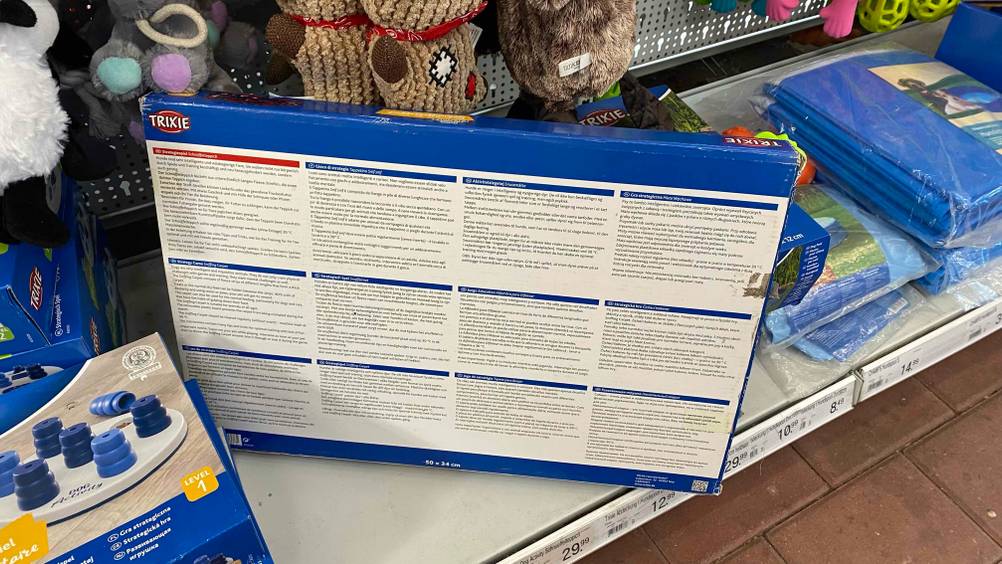 Getestet: Rückseite einer Verpackung eines Schnüffelteppichs auf einem Regal zwischen anderen Produkten und Preisangaben.
