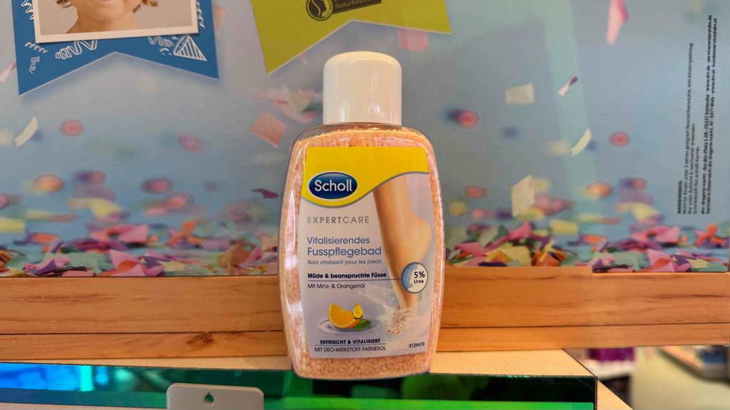 Getestet: Scholl-Fußbadesalz in der Kunststoffflasche steht vor einem Plakat.