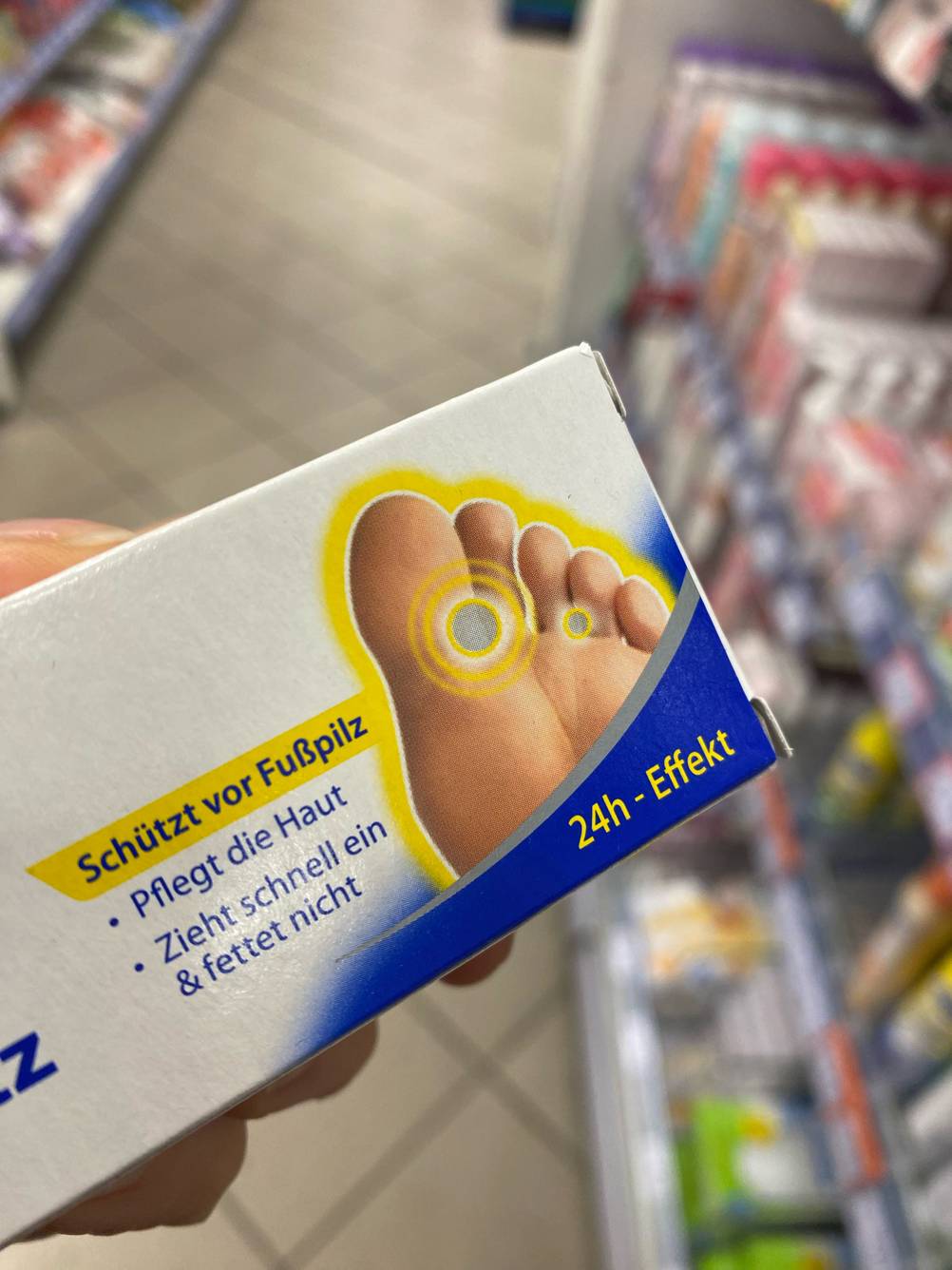 Detailansicht einer Verpackung mit Scholl Fußpilz Creme im Test inklusive Angaben zum Pflegeeffekt, vor einem Verkaufsbereich.