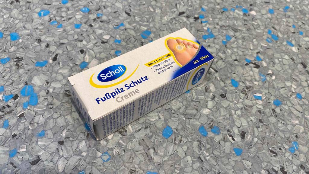 Im Test: Eine Packung Scholl Fußpilz-Creme liegt quer auf grauer Fläche.