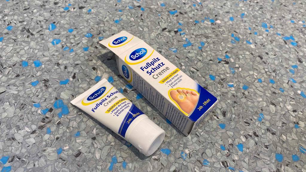 Im Test: Eine Tube Scholl Fußpilz-Creme liegt neben einer offenen Verpackung auf grauer Fläche.