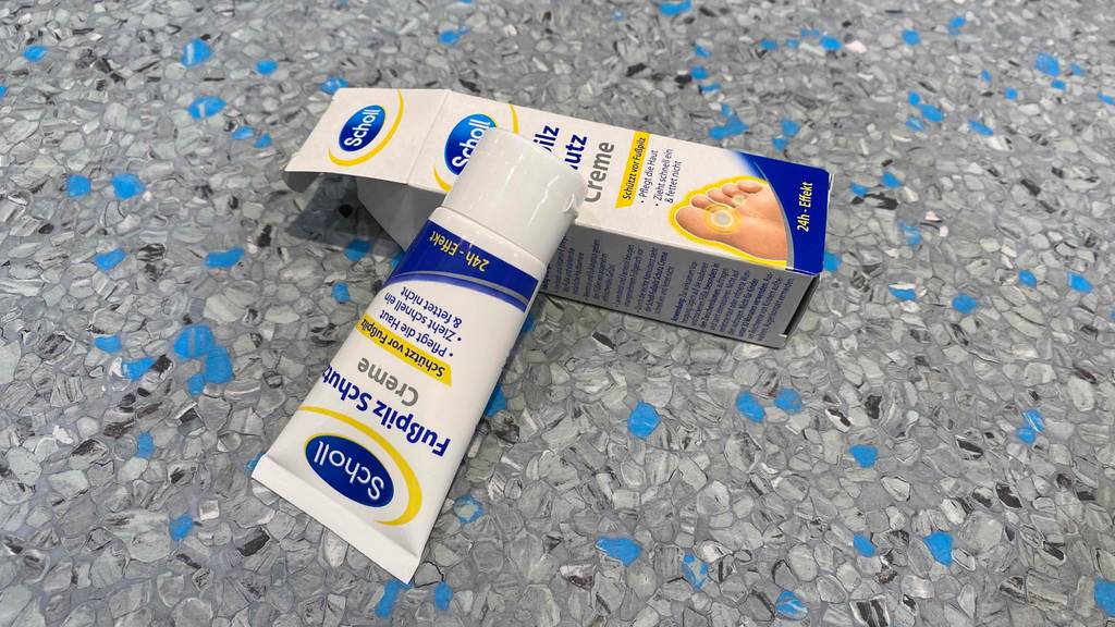 Im Test: Eine Tube Fußpilz-Creme von Scholl liegt quer auf offener Verpackung.