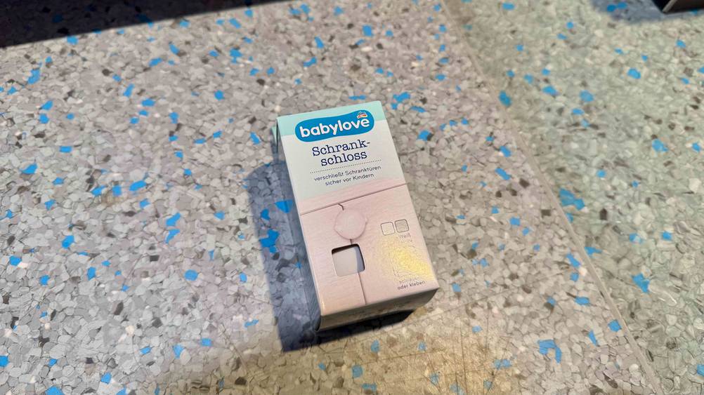Auf einem grauen Boden liegt ein verpacktes Schrankschloss im Test.