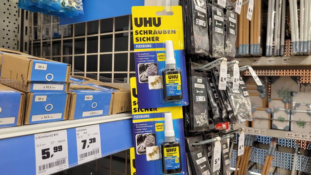 Mehrere Packungen der getesteten Schraubensicherung hängen übereinander an einem Regal.