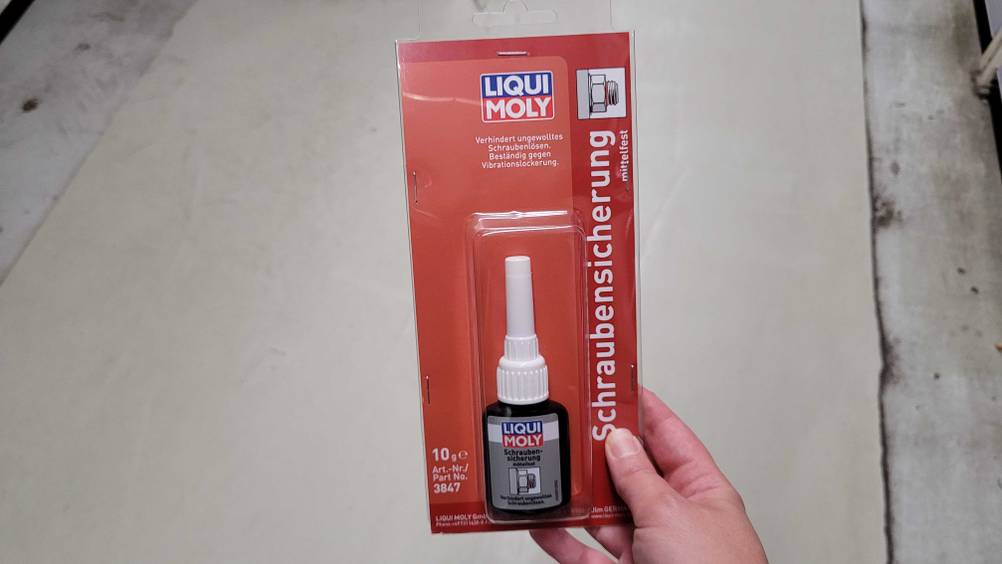 Schraubensicherung im Test: Eine Hand hält ein originalverpacktes Produkt vor einen hellen Boden.