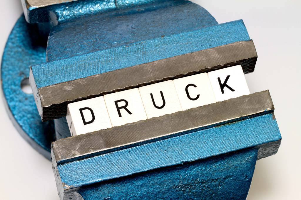 Getesteter drehbarer Schraubstock: ein blauer Schraubstock hält Buchstabenwürfel, die das Wort DRUCK ergeben.