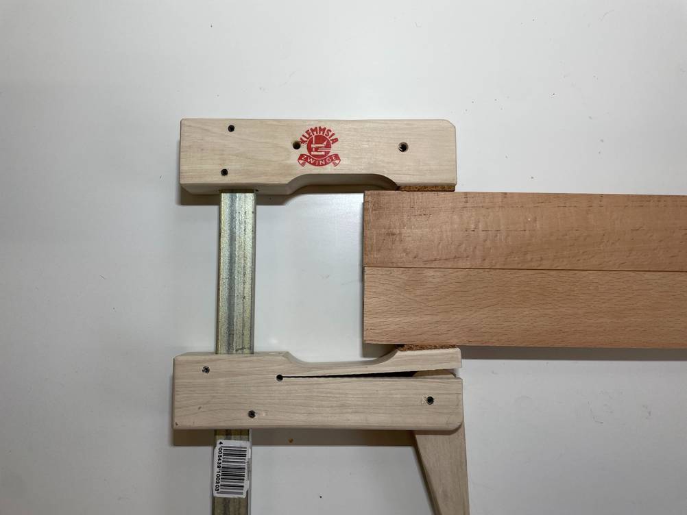 Eine getestete Schraubzwinge befindet sich auf dem Tisch und zwei Holzstücke sind eingeklemmt.