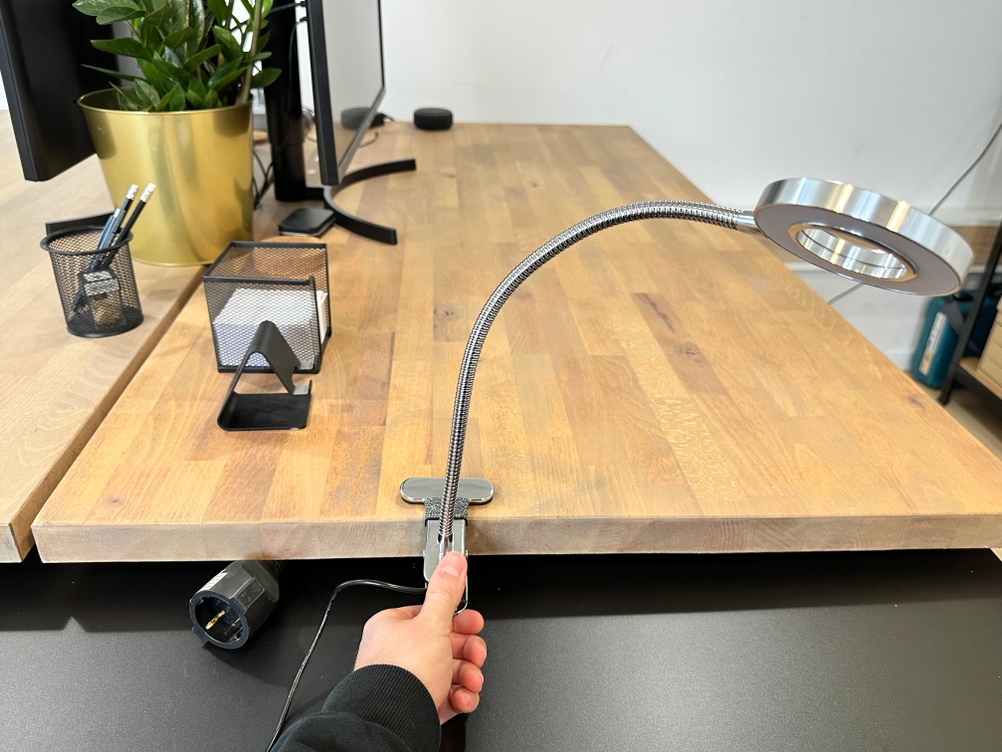 Die Eyocean-LED-Leselampe ist mit ihrer Tischklemme am Holztisch befestigt, während eine Hand den flexiblen Schwanenhals ausrichtet.