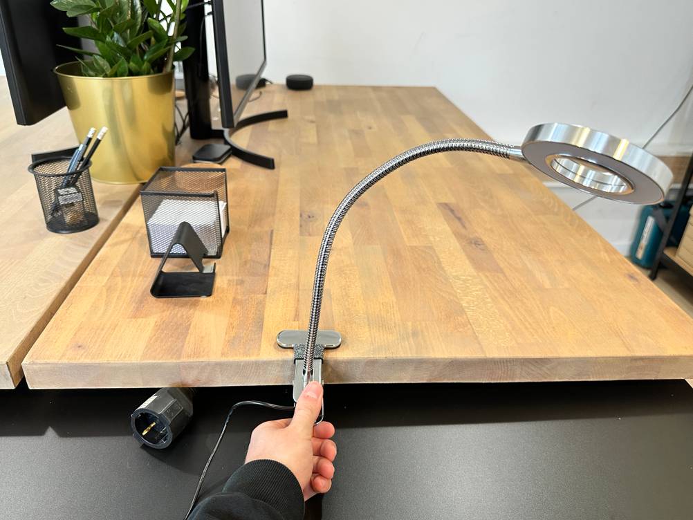 Die Eyocean-LED-Leselampe ist mit ihrer Tischklemme am Holztisch befestigt, während eine Hand den flexiblen Schwanenhals ausrichtet.