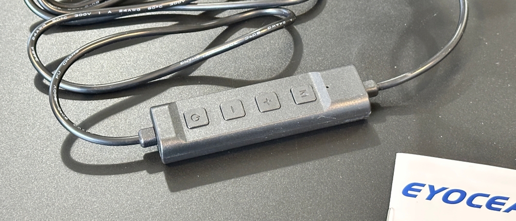 Die Kabel-Fernbedienung der Eyocean-LED-Leselampe mit Tasten für Ein/Aus, Helligkeit und Farbtemperatur liegt auf dem Tisch.