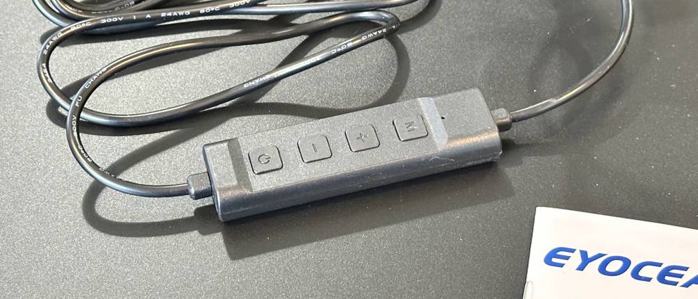 Die Kabel-Fernbedienung der Eyocean-LED-Leselampe mit Tasten für Ein/Aus, Helligkeit und Farbtemperatur liegt auf dem Tisch.