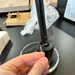 Eine Hand setzt den Innensechskantschlüssel an der Verschraubung zwischen Lampenfuß und Stange der Jukstg HD1906C an.