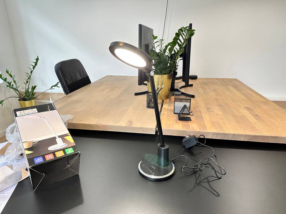 Die Jukstg HD1906C Schreibtischlampe steht angeschaltet auf einem Tisch.