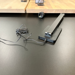 Die Lepro-LED-Schreibtischlampe liegt zusammen mit dem angeschlossenen Netzadapter auf einem schwarzen Tisch und ist noch nicht aufgeklappt.