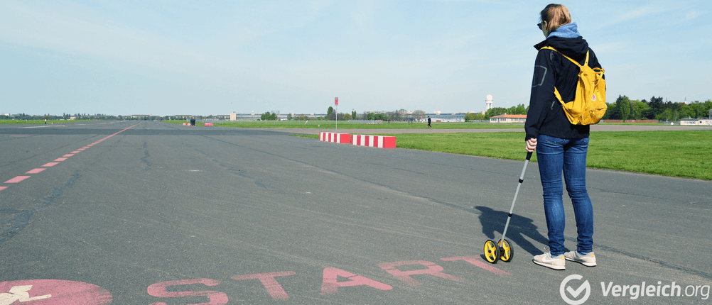 Schrittzähler im Test: Frau mit Rucksack, die eine Distanz auf einer asphaltierten Straße mit einem entsprechenden Messrad ausmisst