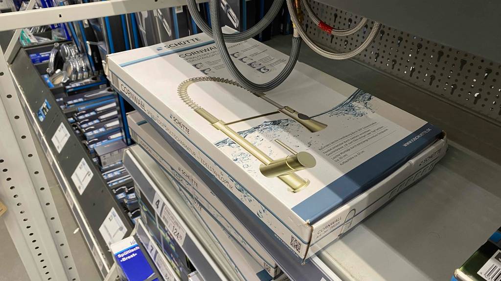 Küchenarmatur-Test: Eine Küchenarmatur in Edelstahloptik der Marke Schütte liegt in ihrer Verpackung auf einem Verkaufsregal unter Anschlussschläuchen.