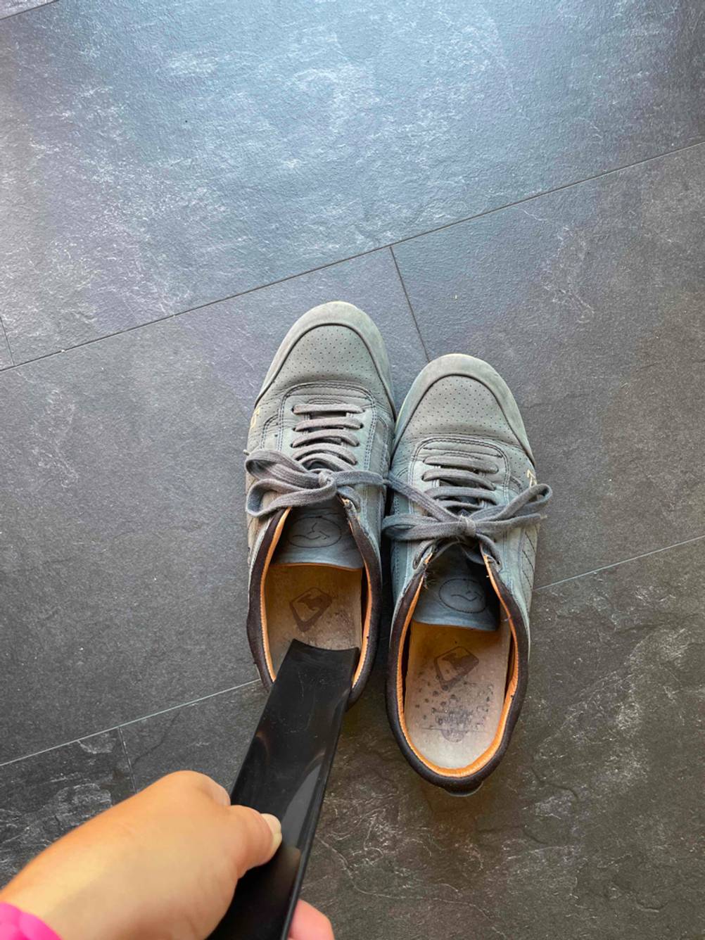 Eine Hand hält einen getesteten Schuhlöffel in einen der beiden nebeneinander stehenden Schuhen.