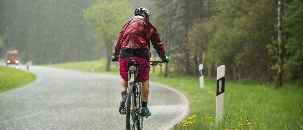 Fahrrad-Schutzblech-Test: Radler fährt bei strömendem Regen auf einer Straße
