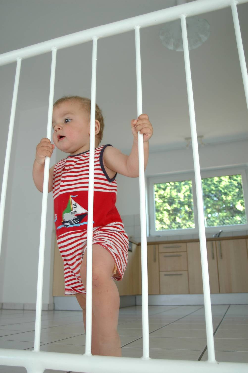 Kaminschutzgitter im Test: ein weißes Kinder-Schutzgitter mit Kleinkind, das sich an den Stäben festhält und durchschaut