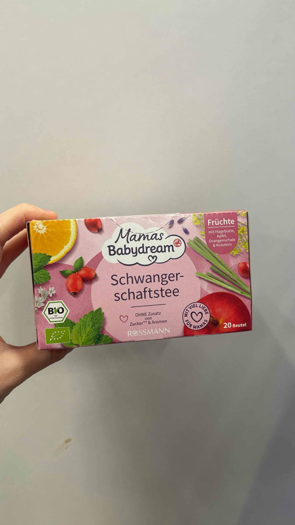 Eine Hand hält den getesteten Schwangerschaftstee vor eine graue Wand.