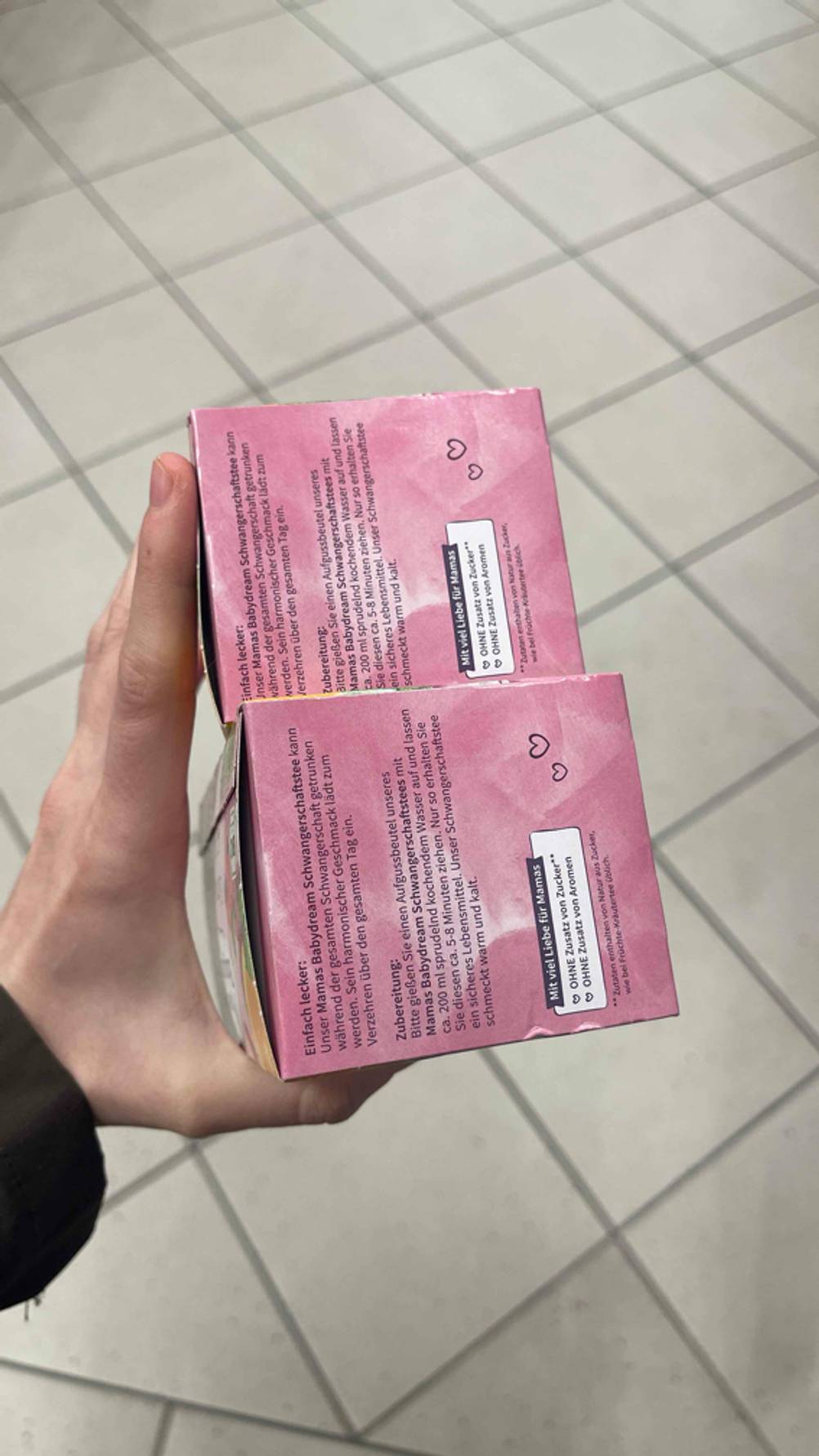 Seitenansicht zweier Packungen des getesteten Schwangerschaftstees von einer Hand gehalten.