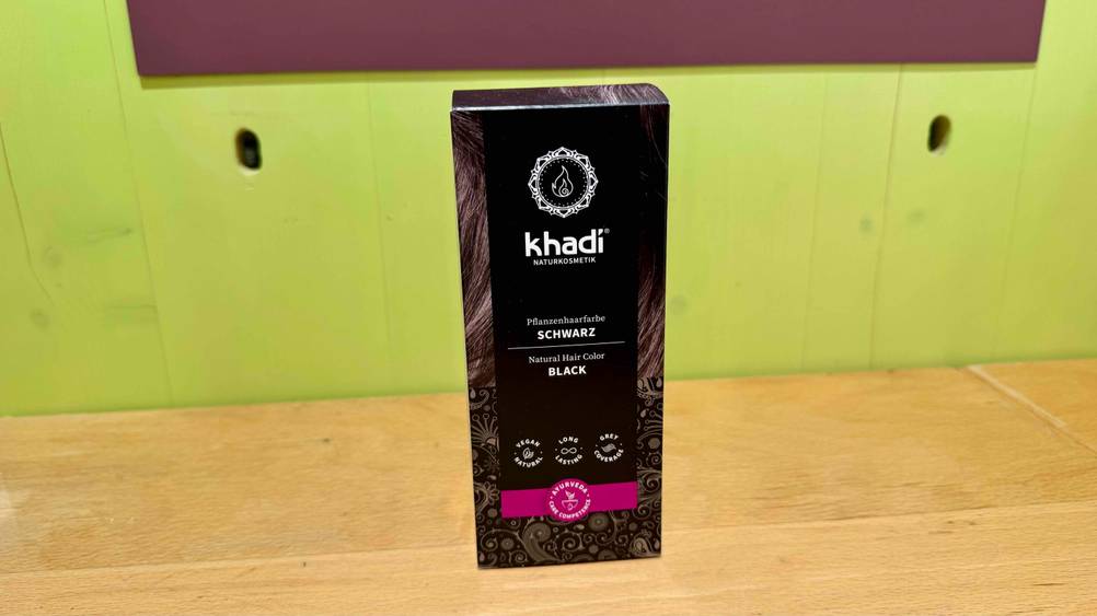Schwarze Haarfarbe im Test: Eine Packung von vorne vor einer grünen Wand.