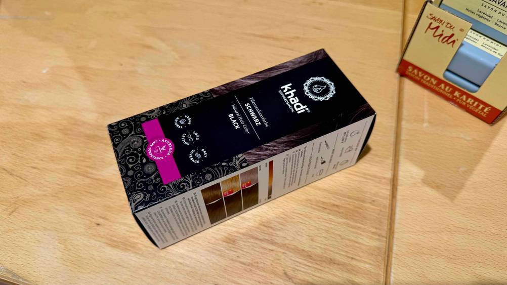 Eine Packung der getesteten schwarzen Haarfarbe liegt schräg auf einer Holzfläche.
