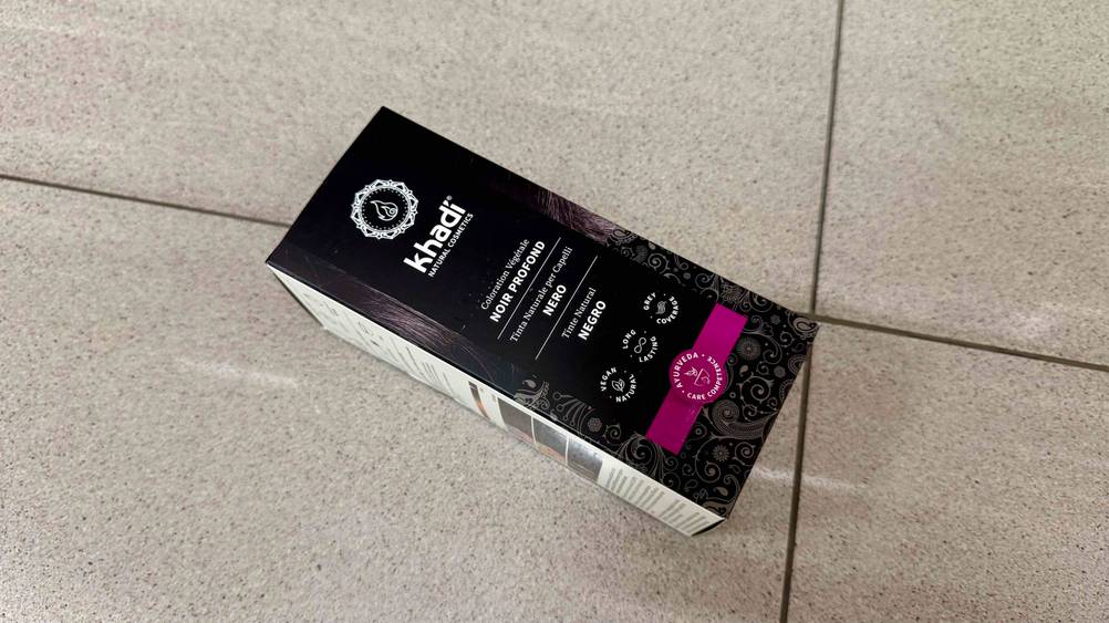 Schwarze Haarfarbe getestet: Eine Packung liegt horizontal auf eine Fließenboden.