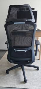 Rückwärtige Ansicht eines schwarz-grauen Bürostuhls im Test, der vor einem Holz-Schreibtisch steht.