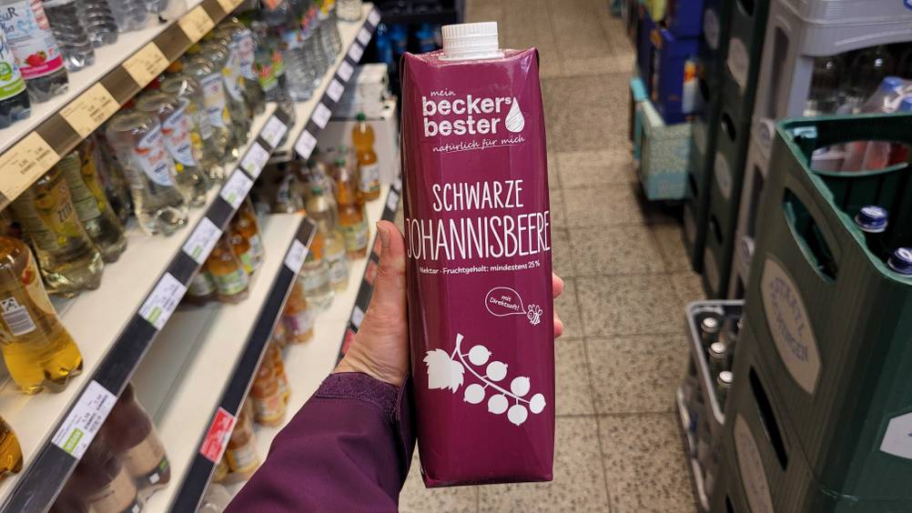 Eine Hand hält eine Packung des getesteten schwarzen Johannisbeersafts hoch.