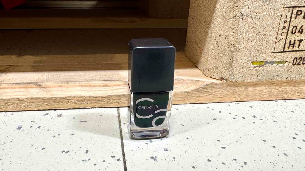 Vor einer Holzpalette auf dem Boden steht eine Flasche des getesteten schwarzen Nagellacks.