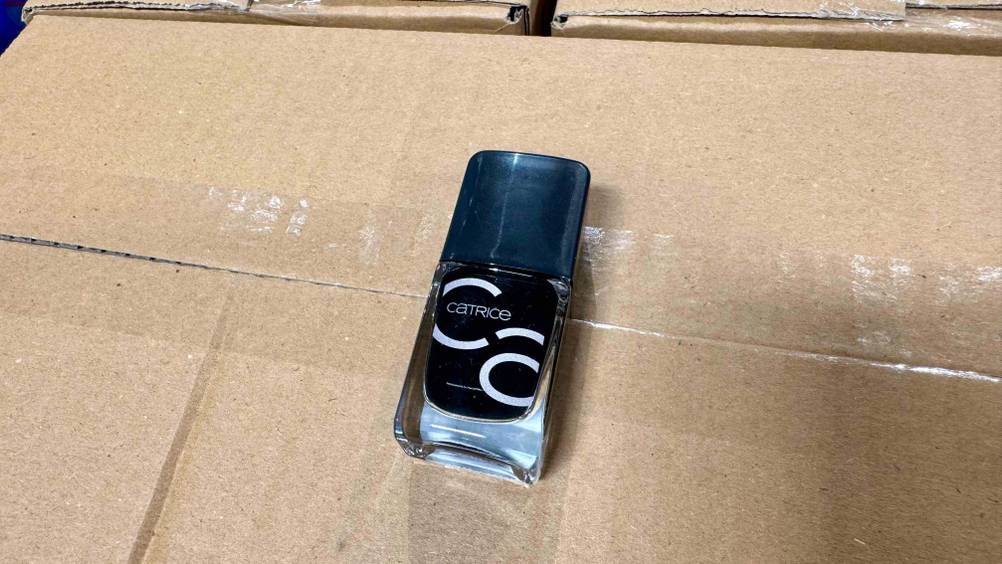 Ein Fläschchen Schwarzer Nagellack von schräg oben auf einem Karton liegend.