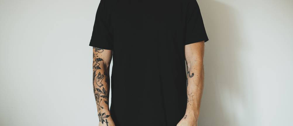 schwarzes-t-shirt-test: Mann mit Tatoos am Arm trägt schwarzes T-Shirt