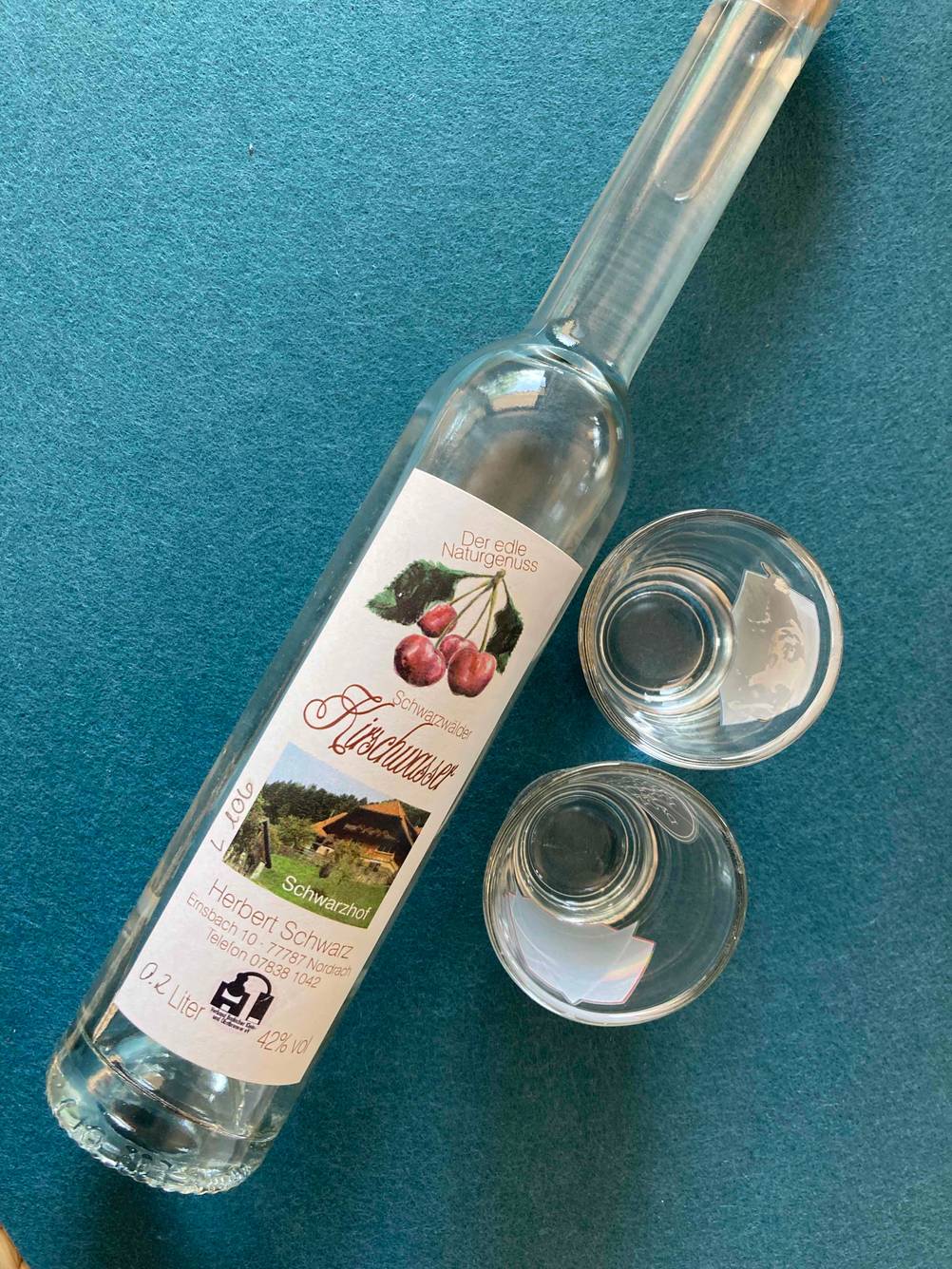 Im Test: Blick von oben auf eine liegende Flasche Kirschwasser, neben der zwei Gläser stehen.